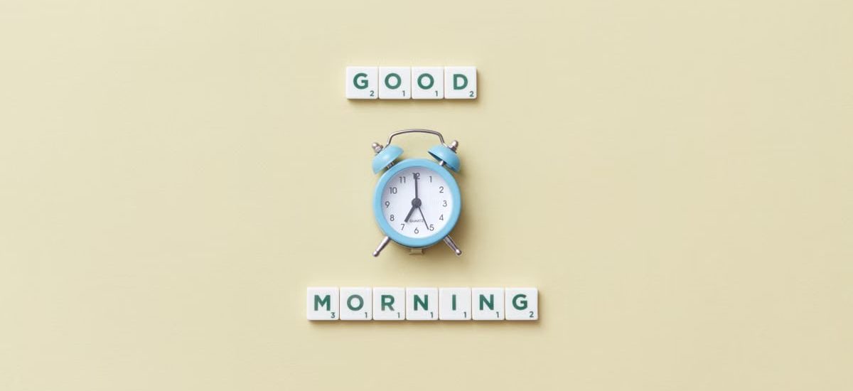 Blue alarm clock with 'Good Morning' scrabble tiles on yellow background.